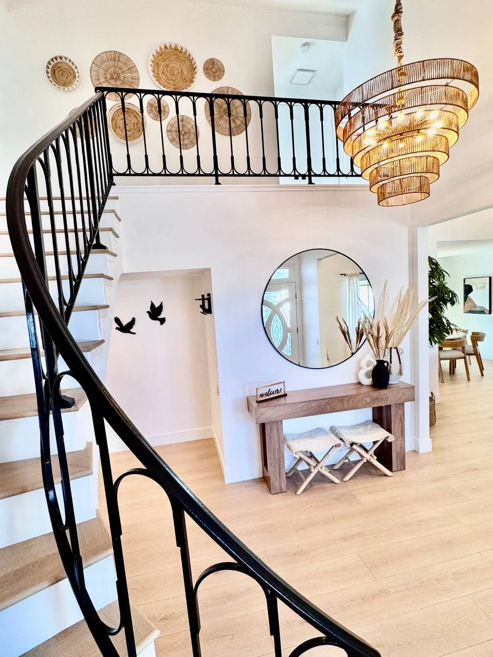 Two-story entryway foyer with curved staircase, rattan chandelier, and round mirror — Sierra residential project by Age of Construction